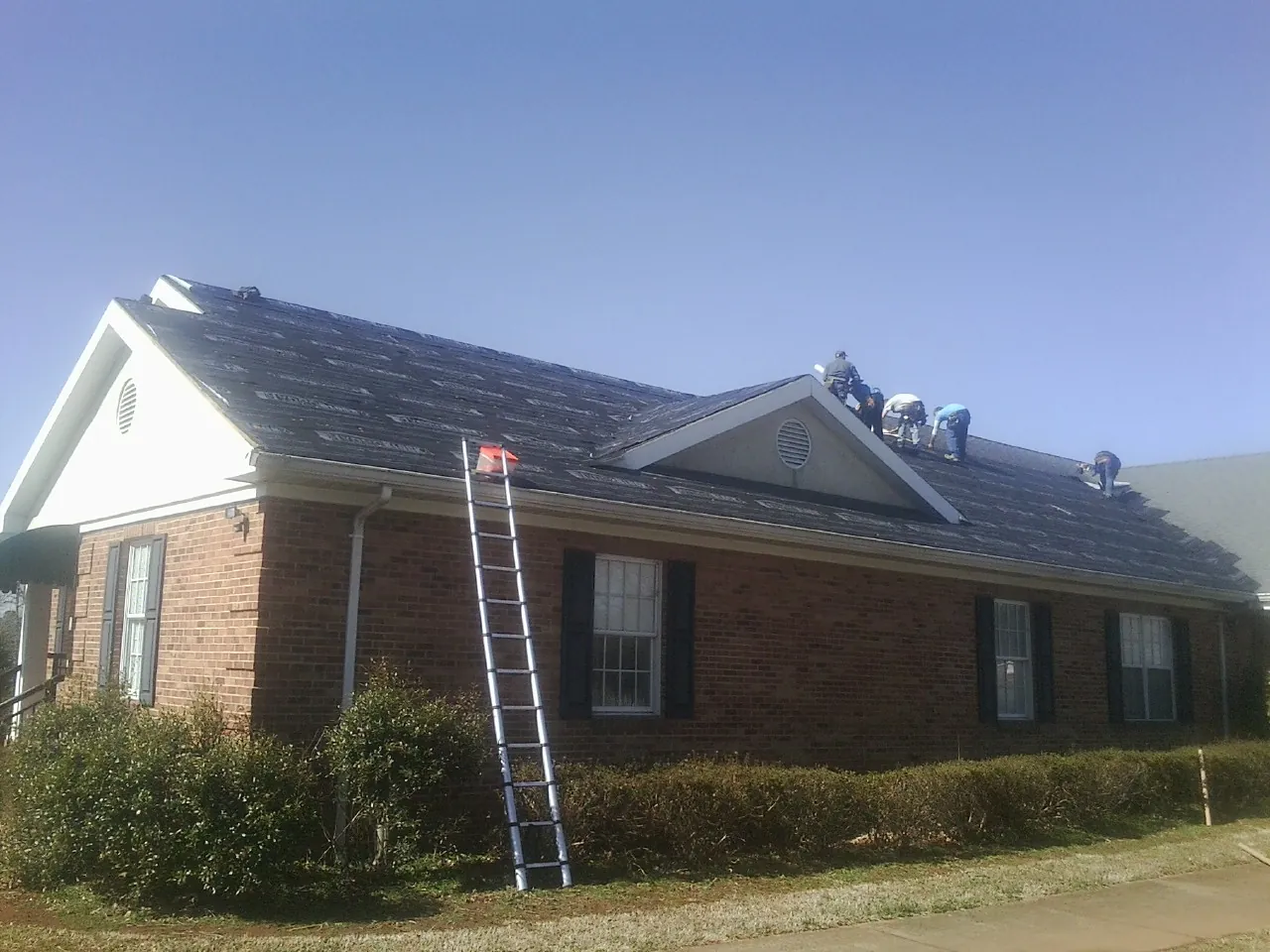 Crew tearing shingles off a brick ranch roof with a ladder set — Emergency Roof Repair work by our crew in Landis