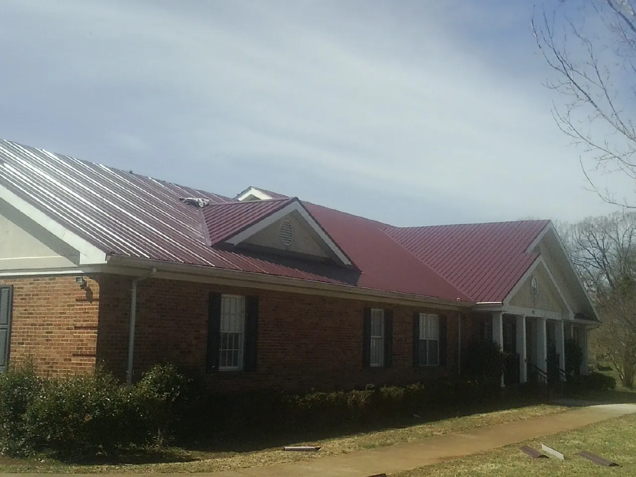 Red metal roof with gabled entries on a long brick building, from a Hail Damage Roof Repair job in Landis