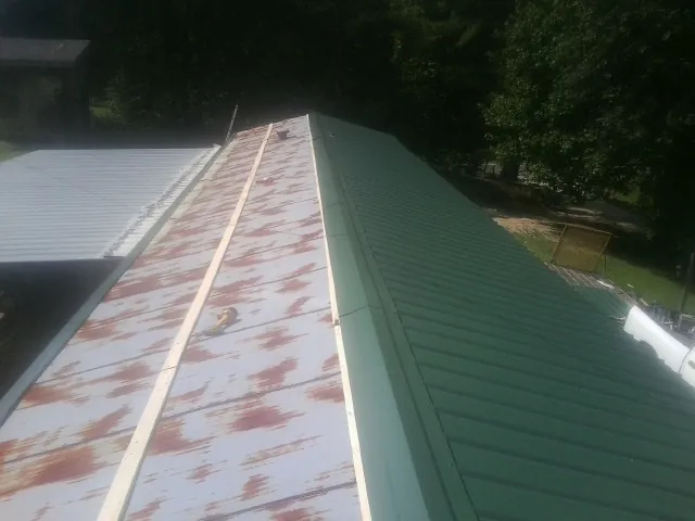 Old rusted panels beside newly installed green metal roofing — Wind Damage Roof Repair by Roofing Brothers in Landis