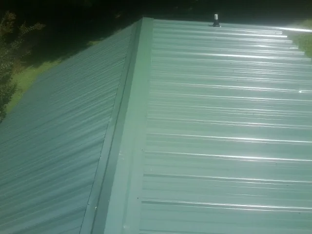 New green metal panels meeting at the ridge of a roof — Flat Roof Repair work by our crew in Landis