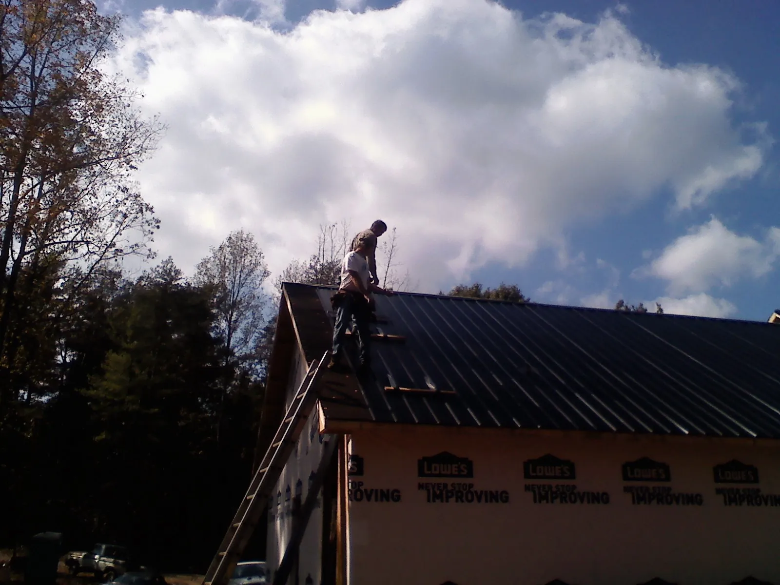 Roofer fastening dark metal panels high against a cloudy sky, from a Roof Inspection job in Landis