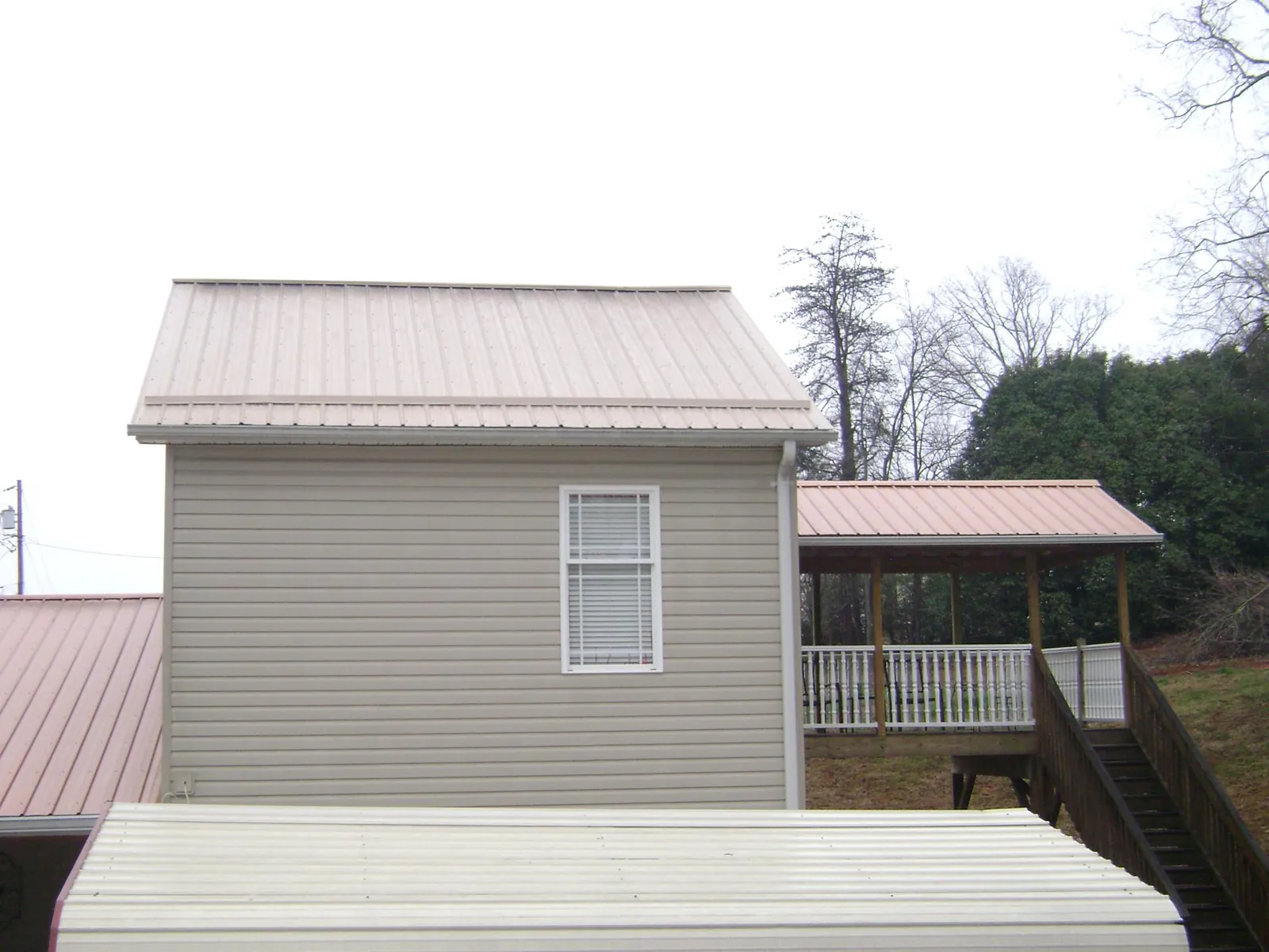 Tan metal roofs on a two story addition and attached porch, from a Roof Replacement job in Landis